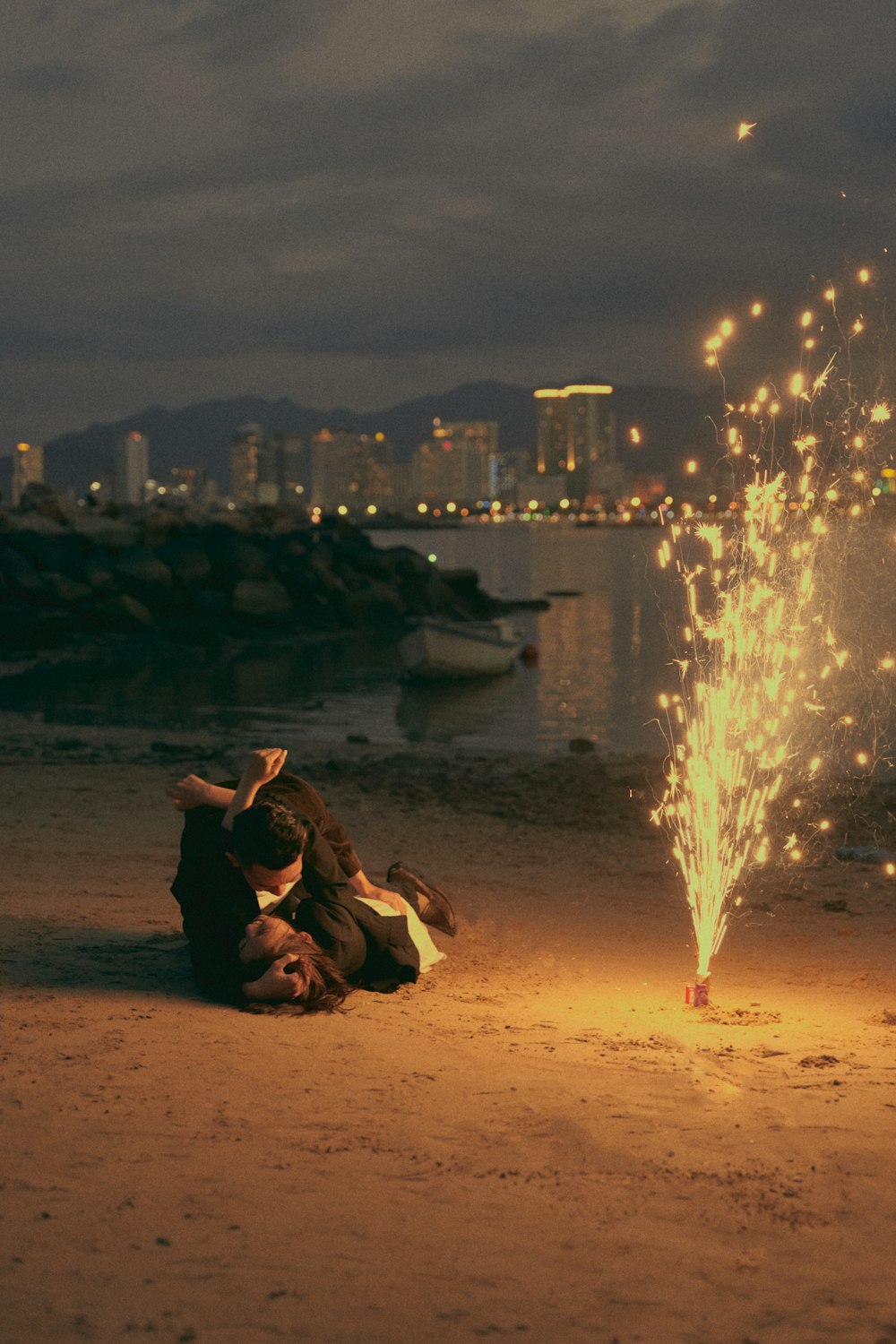 a couple of people sitting on a beach with a city in the background