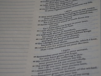 A close-up view of a printed text on a page. The text appears to be part of a religious or literary book, featuring numbered lines and organized in a structured layout. Some text portions are written in bold or have decorative capitals, suggesting emphasis or section headings.