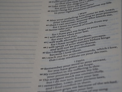 A close-up view of a printed text on a page. The text appears to be part of a religious or literary book, featuring numbered lines and organized in a structured layout. Some text portions are written in bold or have decorative capitals, suggesting emphasis or section headings.