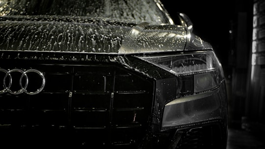 Close-up of a sleek black sports car with water droplets glistening on its polished surface under bright showroom lights.