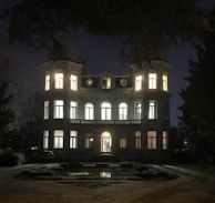 Evening outdoor shot of the mansion illuminated with golden lights and models mingling.