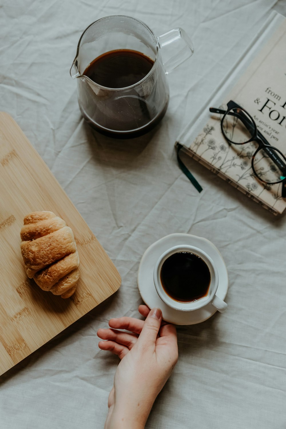 une main tenant une tasse de café à côté d’un plateau de pâtisseries