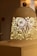 A decorative lamp with intricate cut-out floral and nature patterns, casting warm light. The lamp has a smooth dome shape with a small spherical knob on top, resting on a simple base.