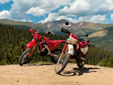 a couple of motorcycles parked on a dirt road with mountains in the background