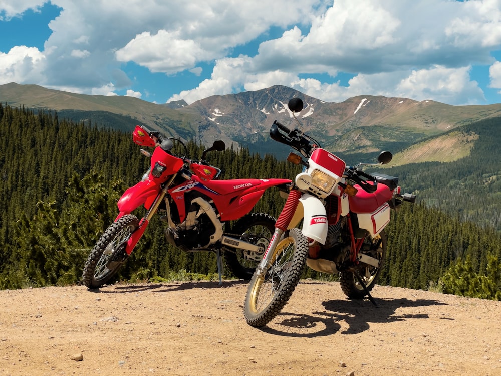 a couple of motorcycles parked on a dirt road with mountains in the background