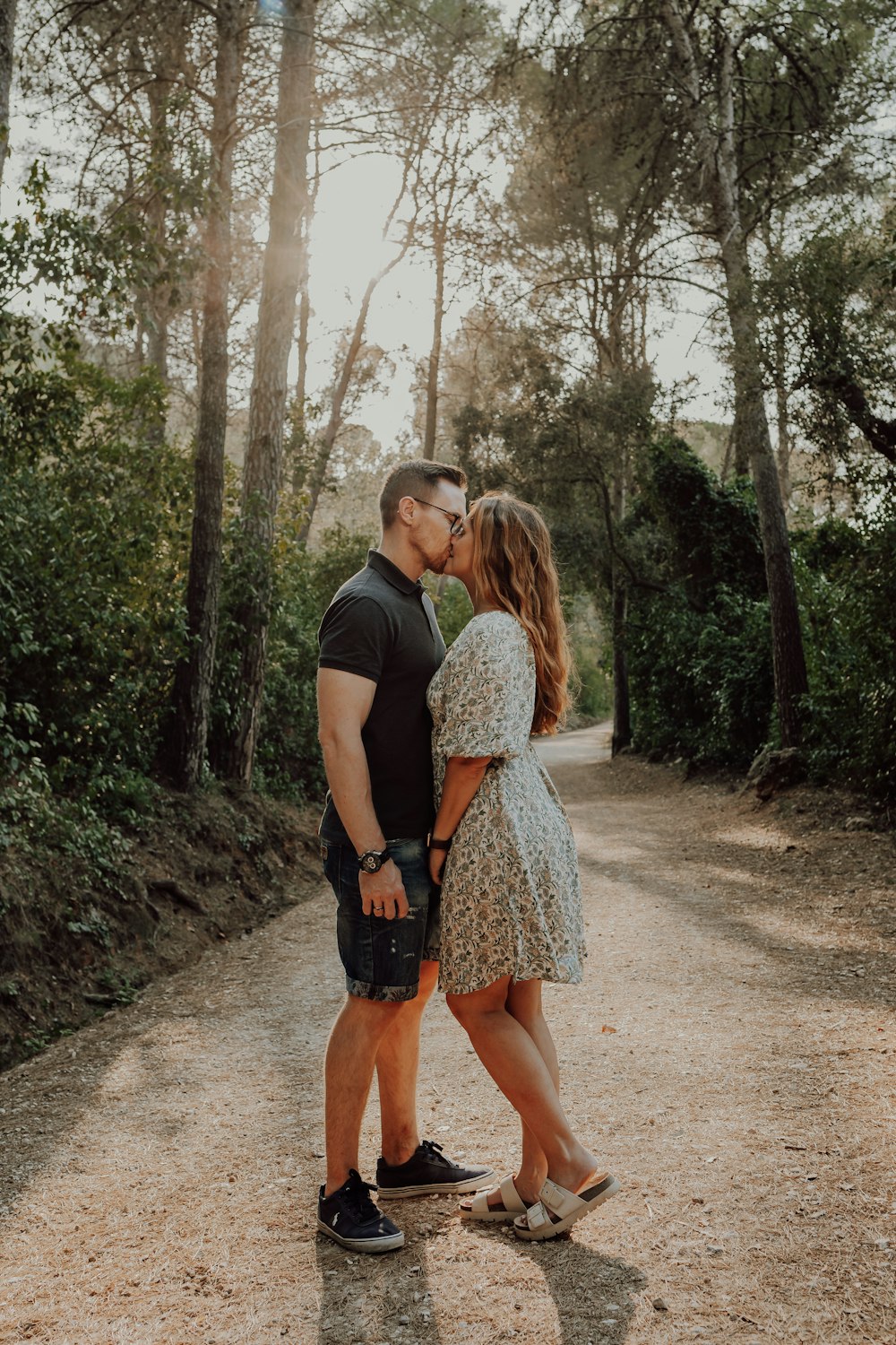 Un hombre y una mujer besándose en un camino de tierra en el bosque