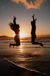 a man and a woman jumping in the air at the beach