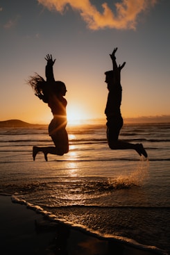 a man and a woman jumping in the air at the beach