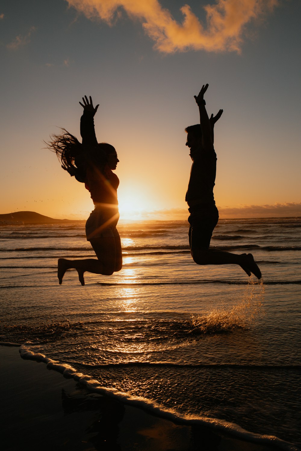 a man and a woman jumping in the air at the beach