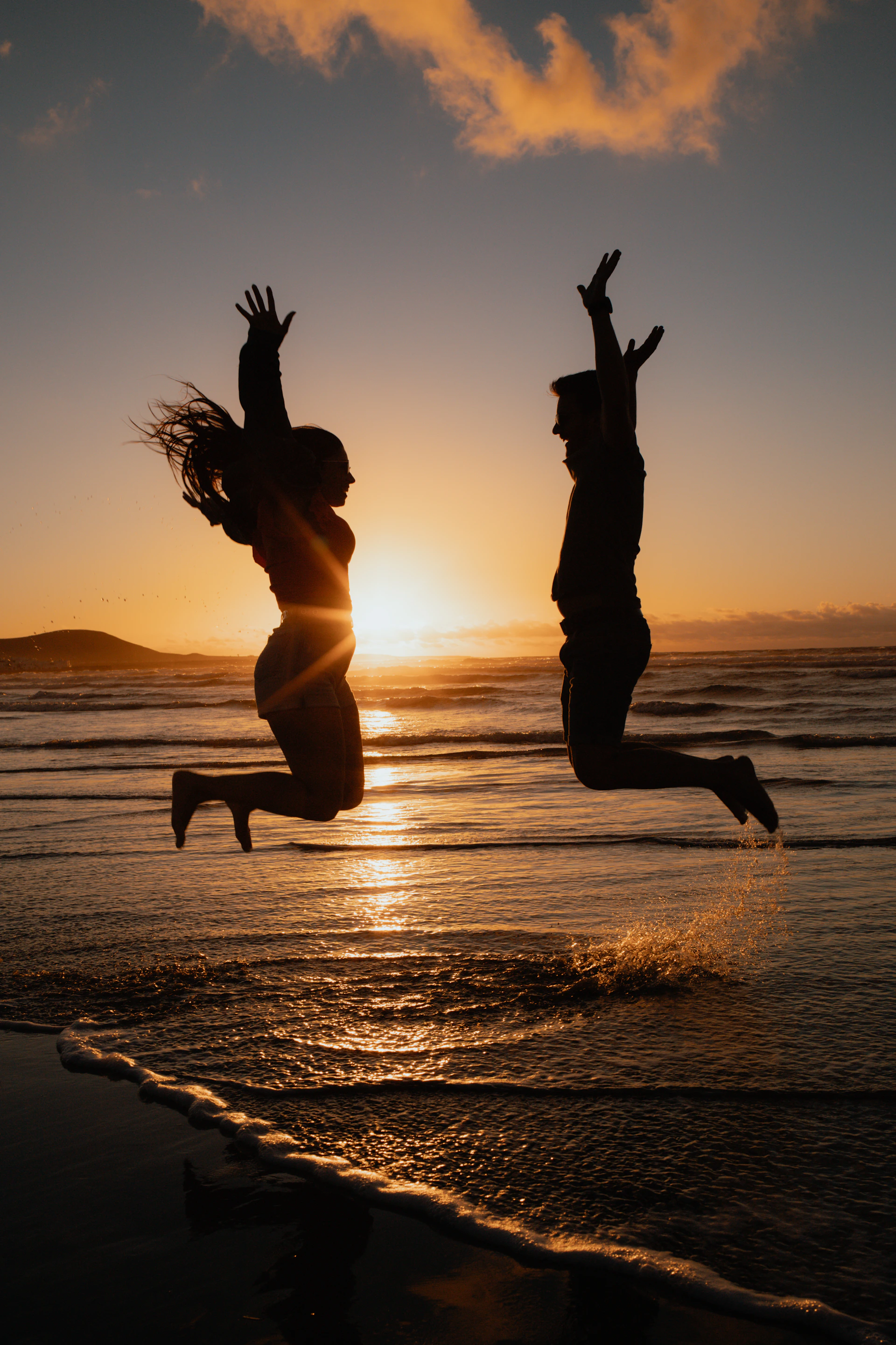 a man and a woman jumping in the air at the beach