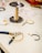 A workspace featuring various jewelry-making tools and materials. A spool of beige thread is placed upright next to a pair of pliers with blue and yellow handles. Several jewelry pieces, including bracelets and small metal components, are scattered on the white surface.