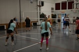 Young students competing in a lively indoor volleyball match with cheering teammates.