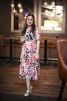 A stylish woman in a chic dress holding a cocktail glass, smiling warmly in a cozy lounge setting.
