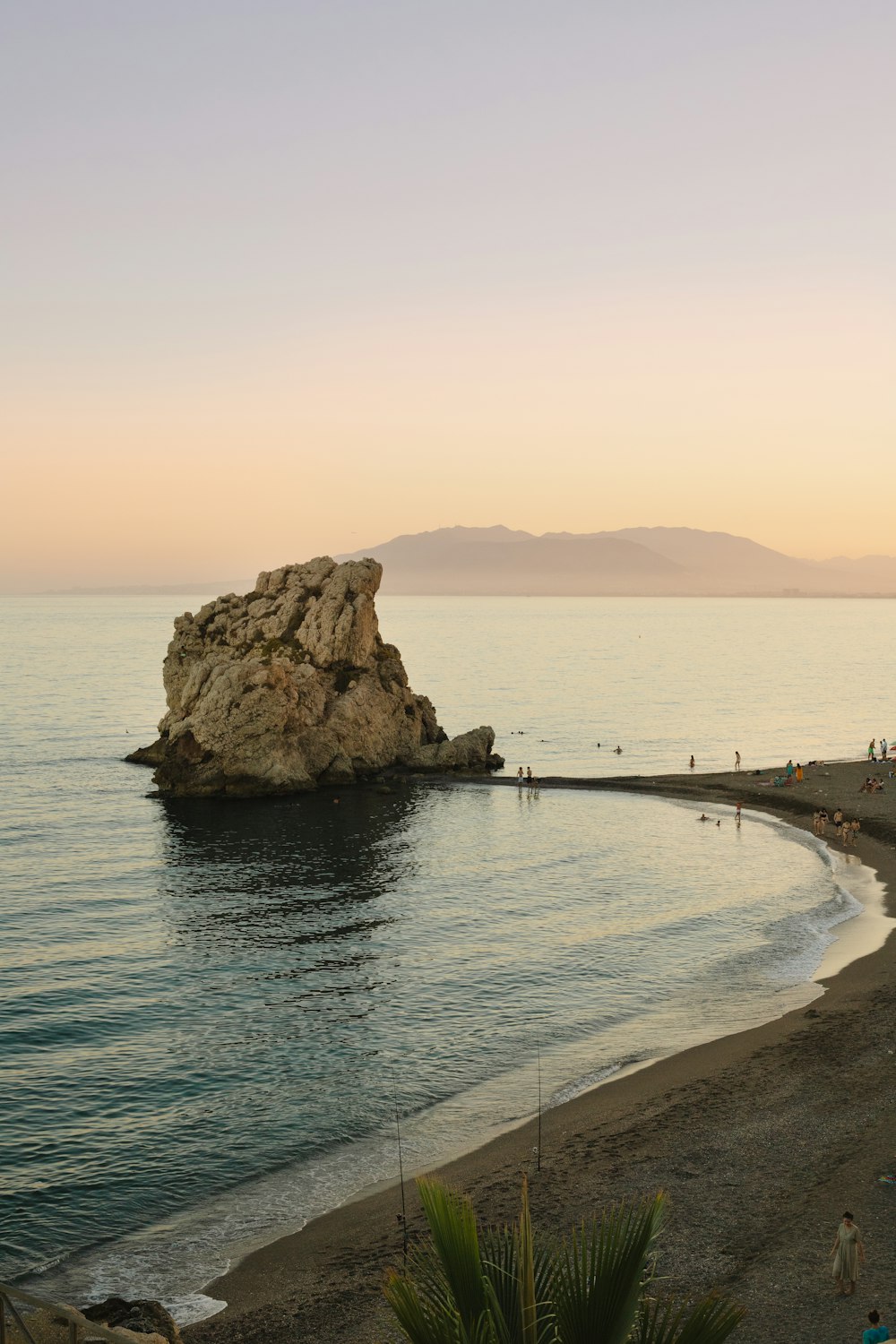 a beach with a large rock in the water