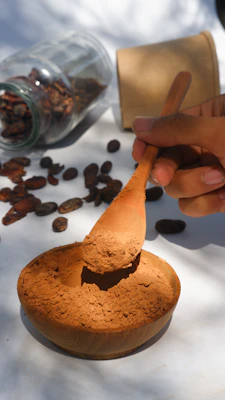 a hand stirring cocao powder with a wooden spoon