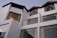Contemporary architecture featuring a white multi-level building with large windows and dark slanted roofs. The structure is modern and minimalistic, exuding a sense of sophistication. Glass balconies and drapes can also be seen through the expansive windows.
