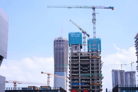 Modern residential buildings under construction with cranes and workers on site during a sunny day.