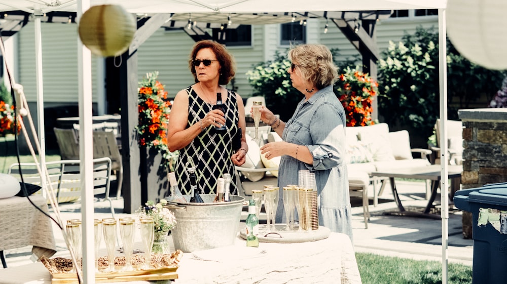 um casal de mulheres de pé ao lado de uma mesa com copos e xícaras