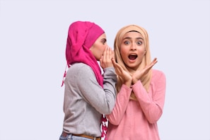 a couple of women wearing pink hoods and holding their hands to their faces
