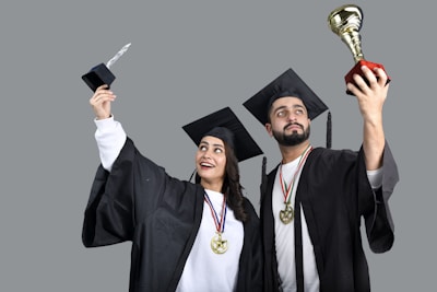 a man and woman wearing graduation gowns and holding a trophy