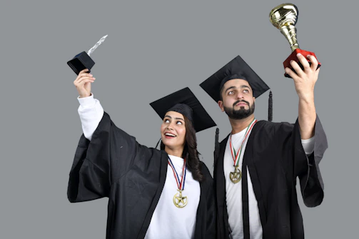 a man and woman wearing graduation gowns and holding a trophy