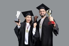 a man and woman wearing graduation gowns and holding a trophy