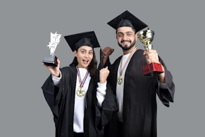 a man and woman wearing graduation gowns and holding a trophy