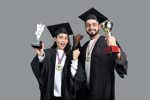 a man and woman wearing graduation gowns and holding a trophy