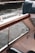 A portion of a boat interior with visible upholstery and a wooden armrest, partially overlooking a body of water with gentle ripples. The water is bordered by a concrete edge and metal railing.