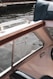 A portion of a boat interior with visible upholstery and a wooden armrest, partially overlooking a body of water with gentle ripples. The water is bordered by a concrete edge and metal railing.