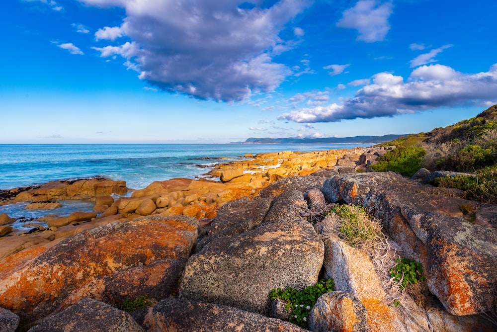 a rocky beach with blue water and clouds