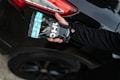 A hand holding a packaged product labeled 'CHU' is positioned near the rear light of a black car with a shiny surface. The product packaging features a combination of black, white, and turquoise colors. An arm dressed in a black long-sleeved garment extends towards the vehicle.