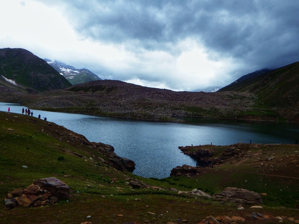 a body of water with people walking on it by mountains