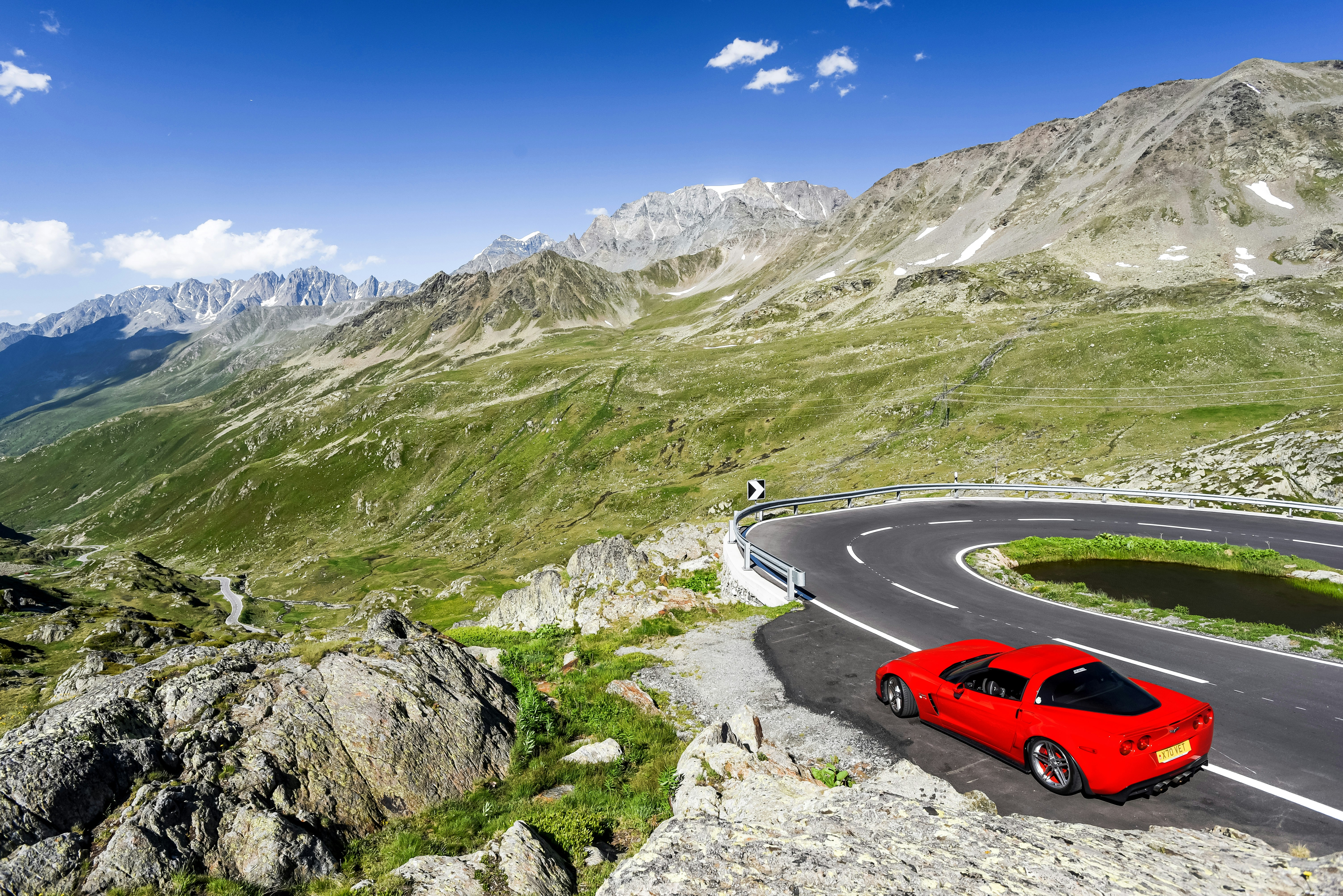 a red car driving on a road in the mountains