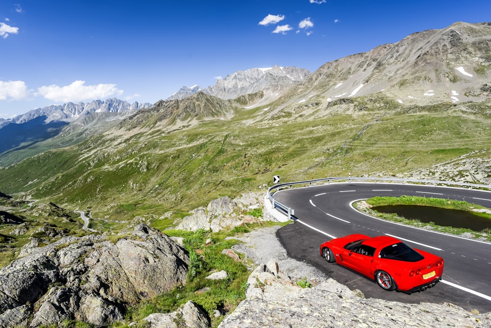 a red car driving on a road in the mountains