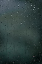 Water droplets cover a transparent surface, likely glass, with a slightly blurred background.