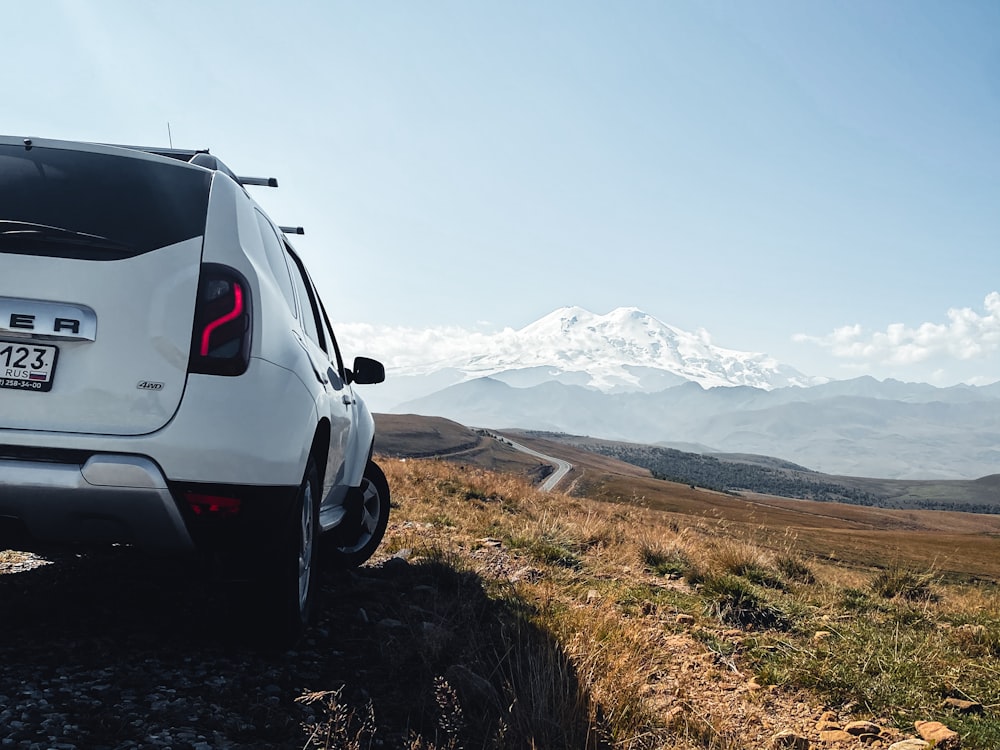 a white car parked on a dirt road with a snowy mountain in the background