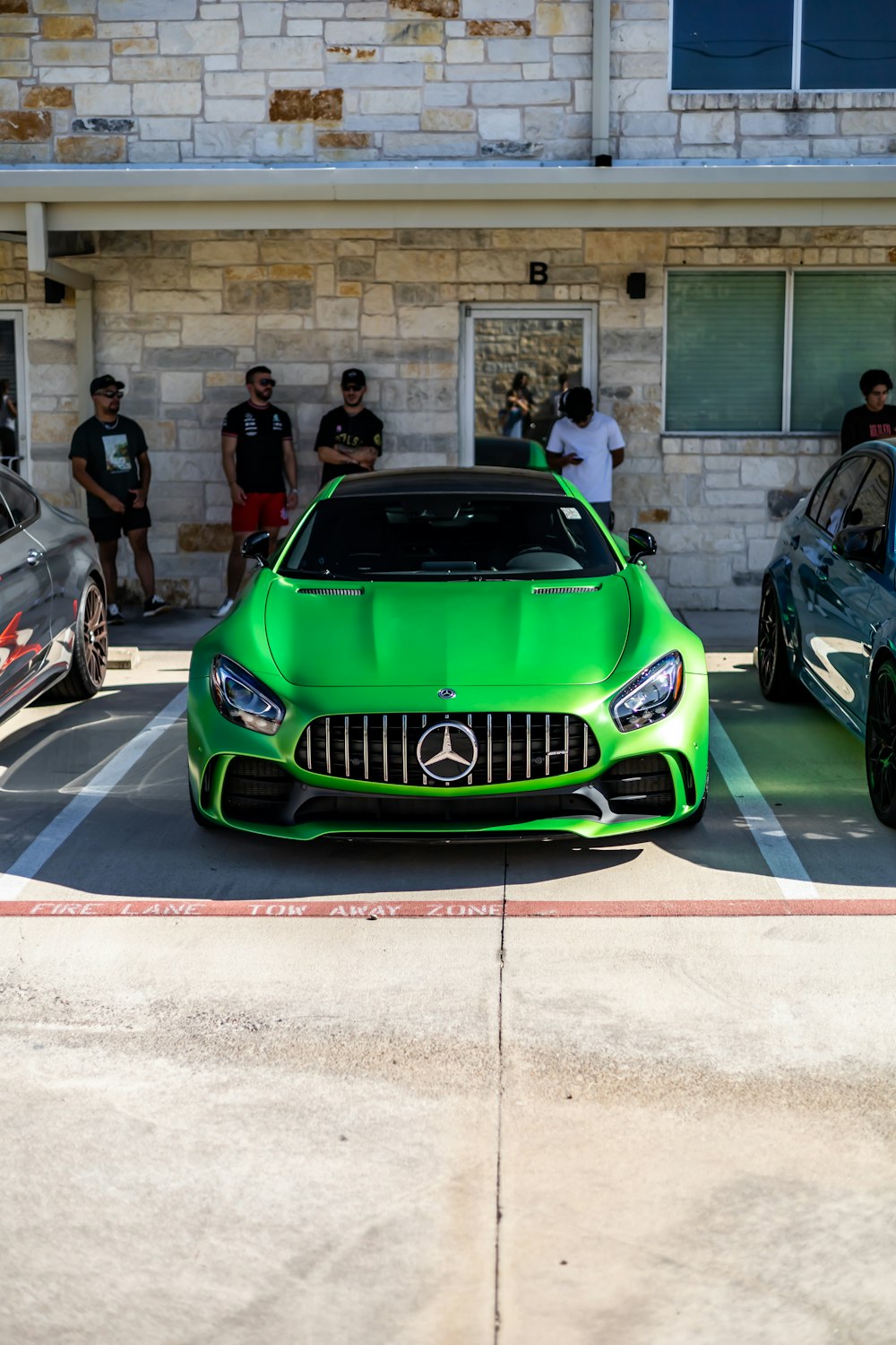 a green sports car parked in front of a building with people standing around