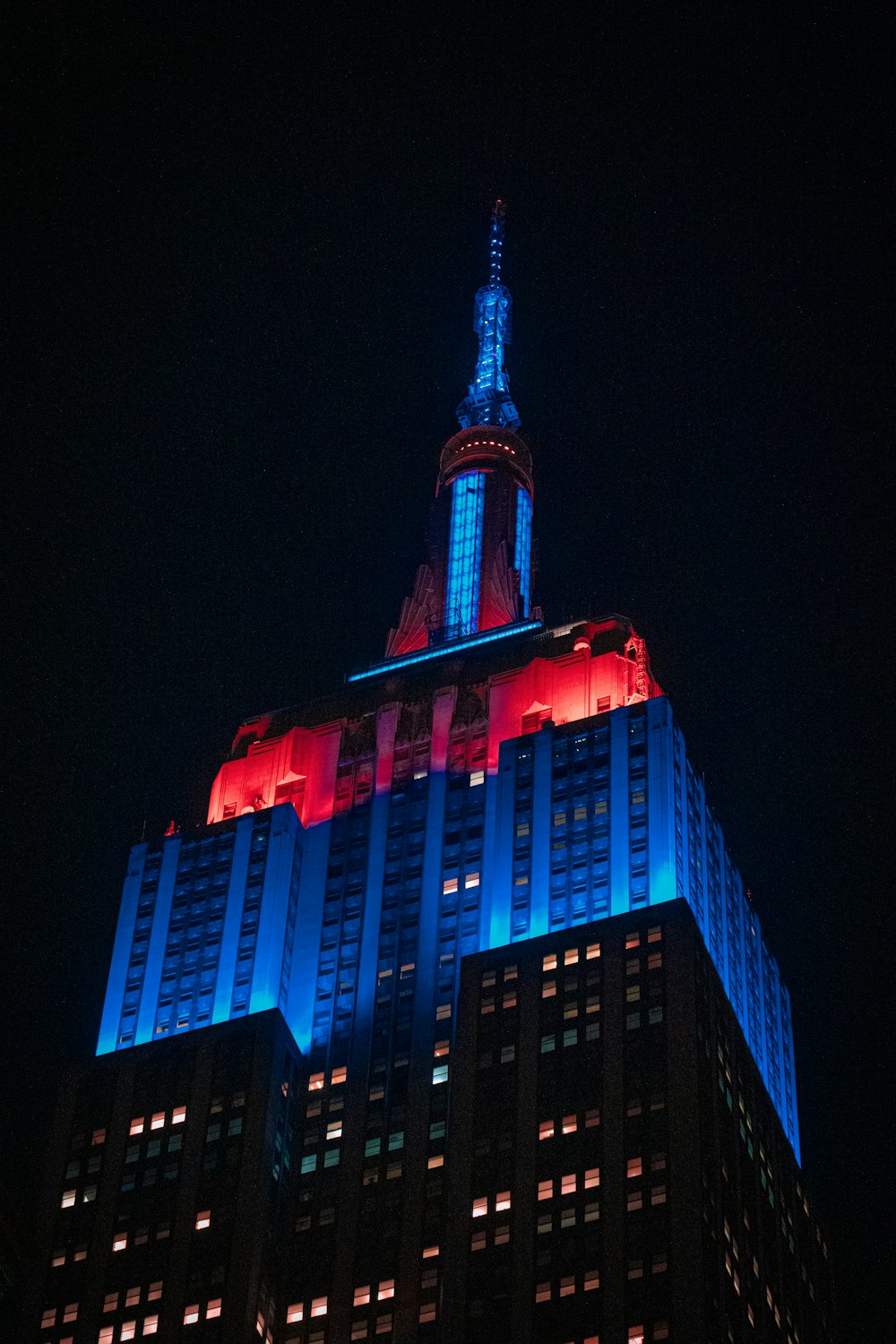 a tall building with a blue top with Empire State Building in the background