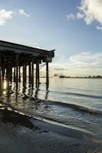 A serene coastal scene showing gentle waves lapping against a wooden pier at sunrise.