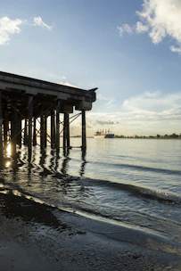 A serene coastal scene showing gentle waves lapping against a wooden pier at sunrise.