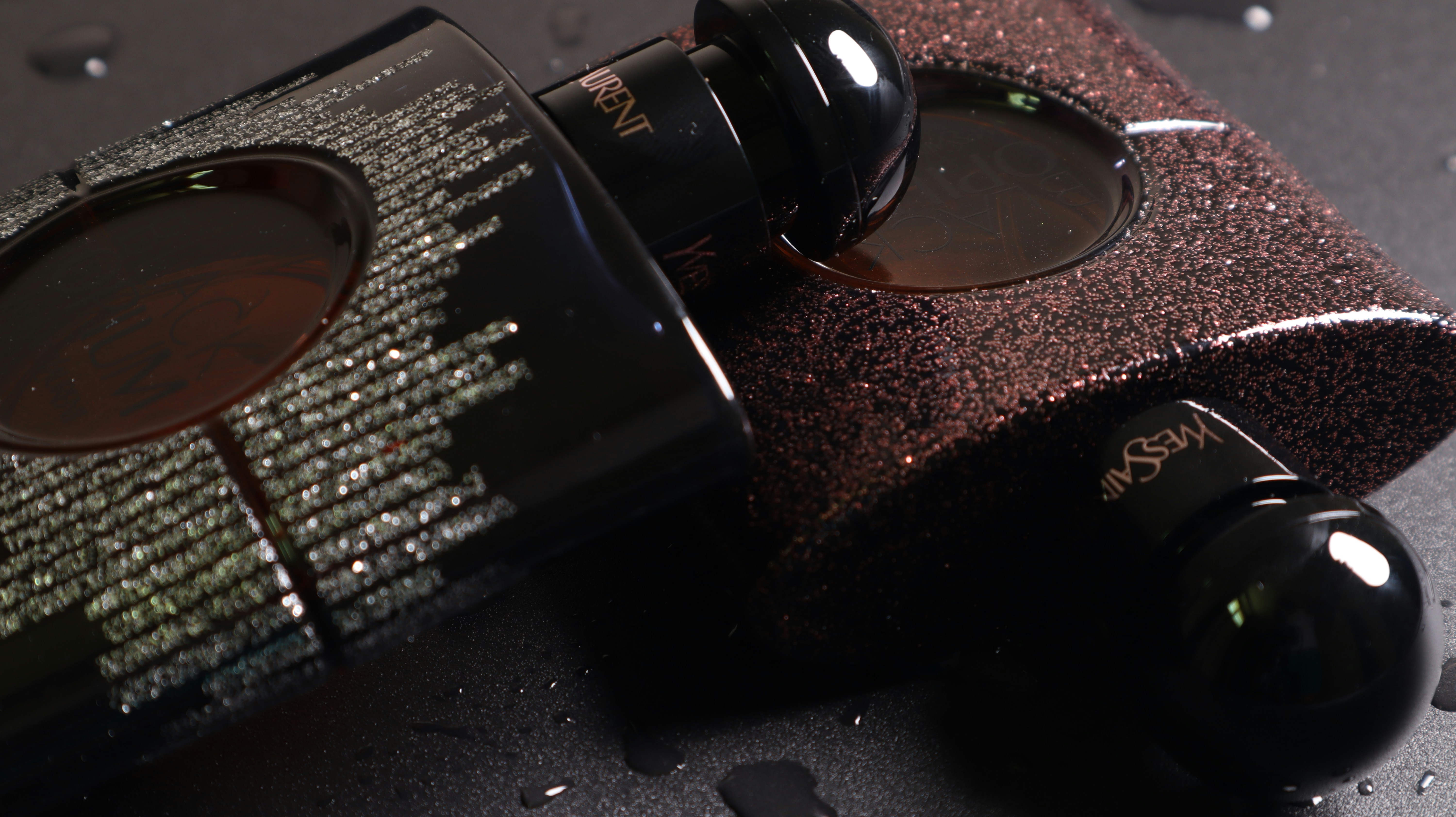 YSL Black Opium dark bottle with golden glitter cap on a black velvet surface with dramatic lighting