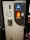 A bottle recycling machine with a slot for inserting bottles, a circular sign indicating recycling, and a lit display. An information sheet with text in a foreign language is attached to the front.