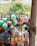A street vendor selling a variety of colorful plastic household items from the back of a small truck. Various kitchenware and containers, including baskets, buckets, and strainers, are stacked and hung for display. A young boy stands nearby, observing the items.