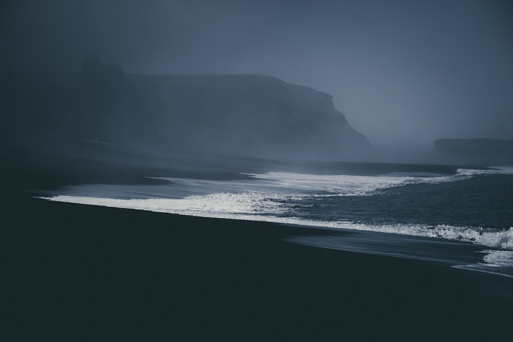 a beach with waves and a large rock in the background