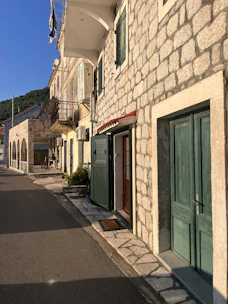 Sunlit stone house with green shutters nestled in a quiet Grottole alley.