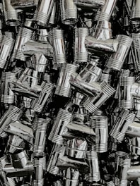 A dense collection of shiny, metallic pipe fittings with threaded sections. The fittings have reflective surfaces and are stacked in an organized, overlapping fashion.