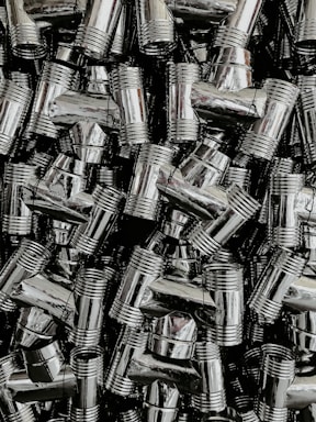 A dense collection of shiny, metallic pipe fittings with threaded sections. The fittings have reflective surfaces and are stacked in an organized, overlapping fashion.