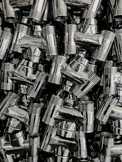 A dense collection of shiny, metallic pipe fittings with threaded sections. The fittings have reflective surfaces and are stacked in an organized, overlapping fashion.