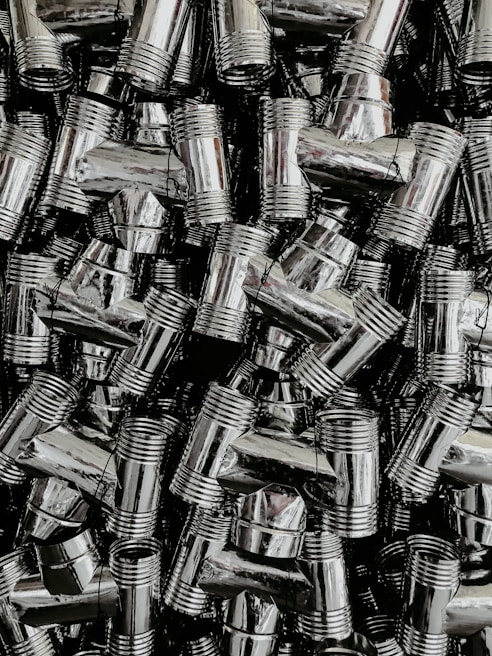 A dense collection of shiny, metallic pipe fittings with threaded sections. The fittings have reflective surfaces and are stacked in an organized, overlapping fashion.